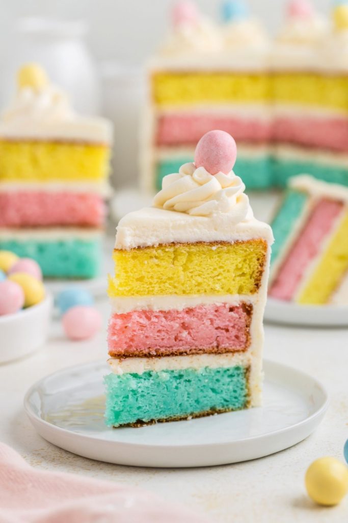 Slice of colorful Easter layer cake topped with butter cream and Easter egg. 