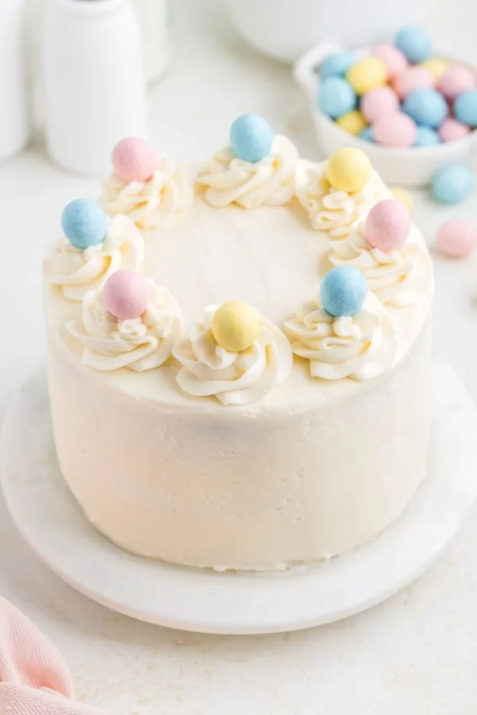 Three layer cake covered in butter cream topped with colorful mini Easter eggs. 