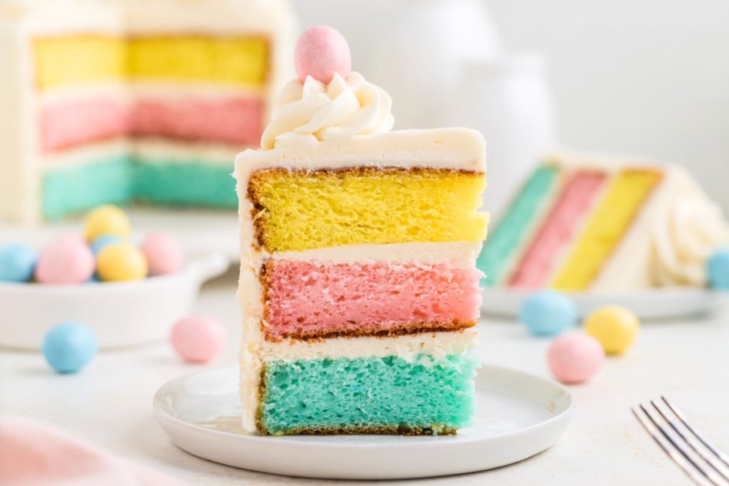 Blue, pink and yellow layer cake topped with buttercream frosting and a pink candy egg. 