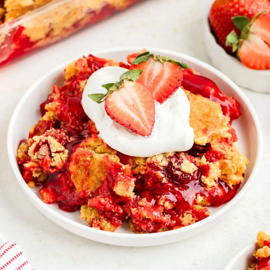 Easy strawberry dump cake made with just three simple ingredients topped with whipped cream.
