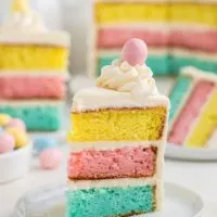 Slice of colorful Easter layer cake topped with butter cream and Easter egg.