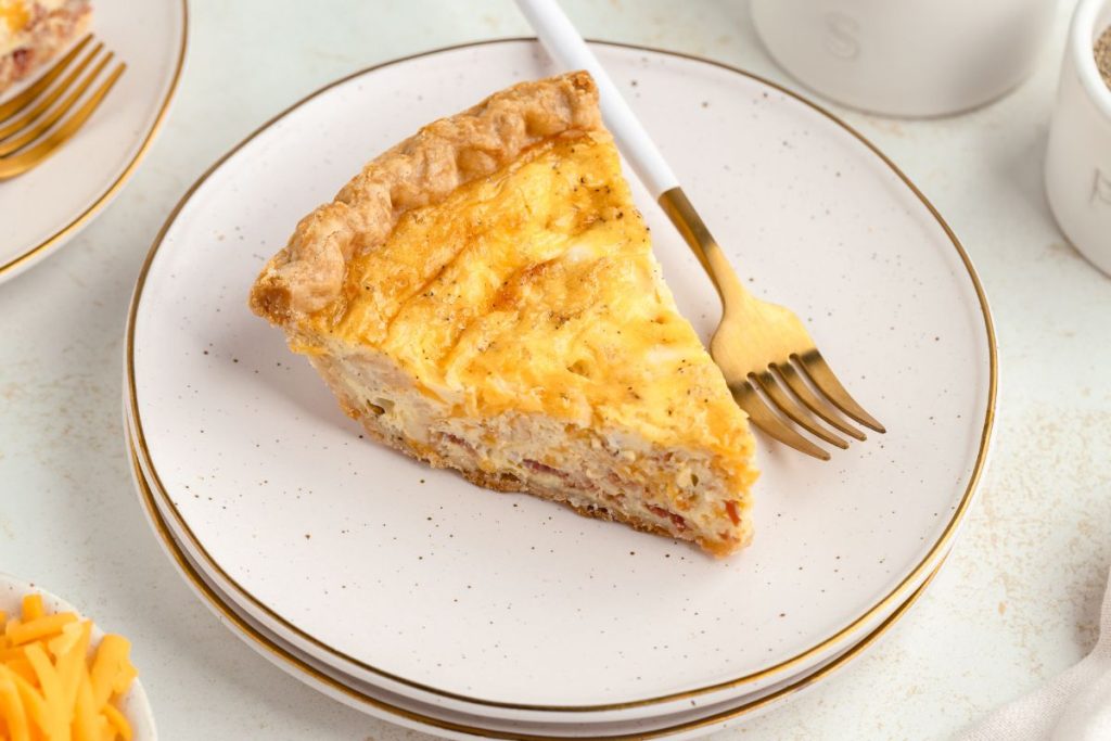 Egg, bacon, and cheddar quiche with pie crust on a plate. 