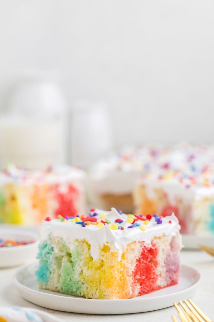 Slice of colorful jello poke cake topped with Cool Whip. 