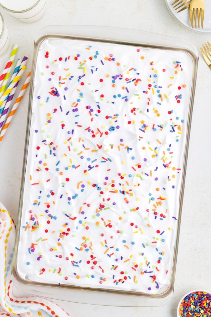 Cake in a 9x13 inch pan topped with Cool Whip and rainbow sprinkles. 