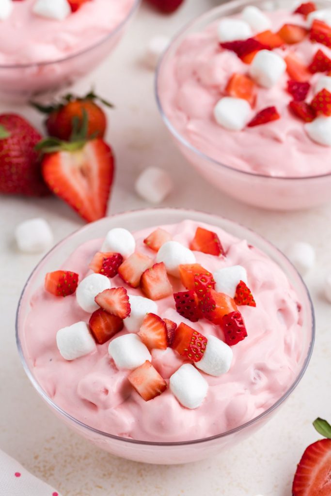 Three bowls full of creamy strawberry fluff dessert with fresh strawberries and mini marshmallows.