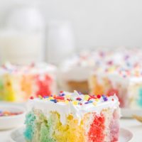 Slice of colorful jello poke cake topped with Cool Whip.