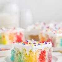 Slice of colorful jello poke cake topped with Cool Whip.