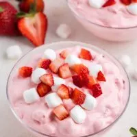 Three bowls full of creamy strawberry fluff dessert with fresh strawberries and mini marshmallows.