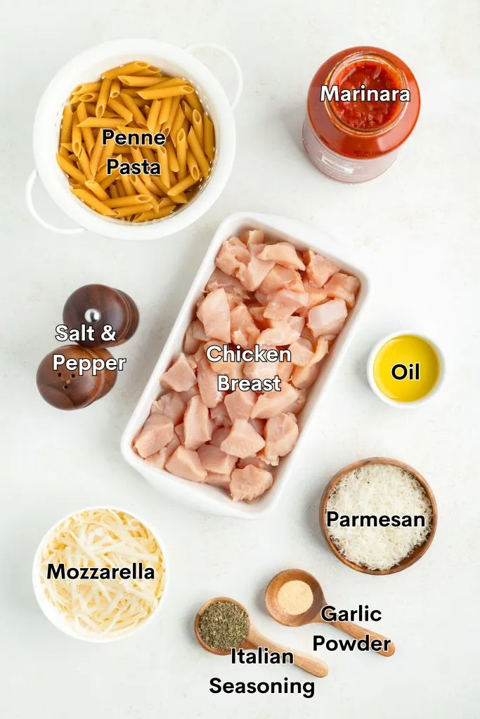 Ingredients such as chicken, pasta, tomato sauce, cheese, and seasonings laid out on the counter. 