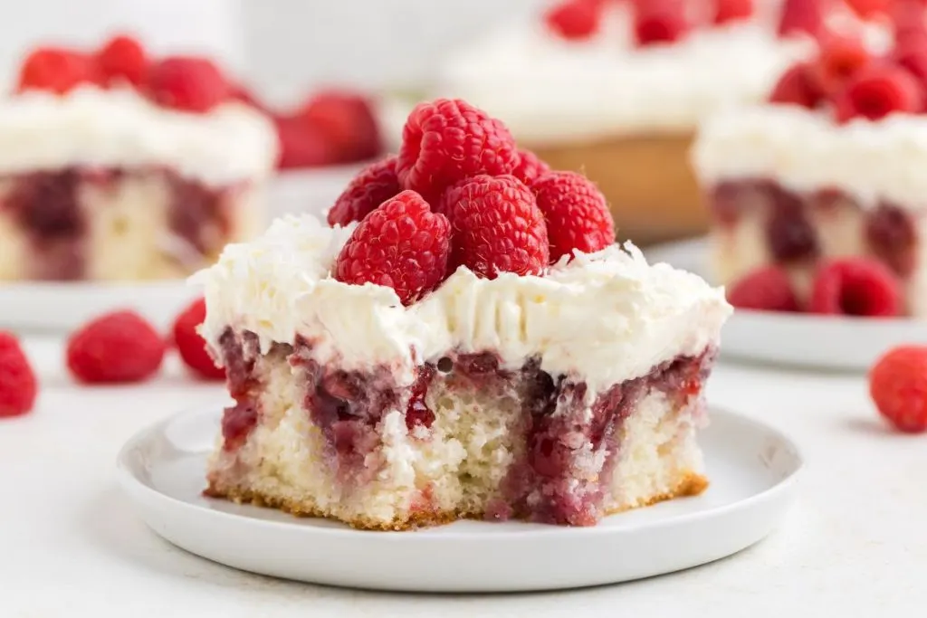 Slice of raspberry coconut poke cake with a bite missing on a plate.