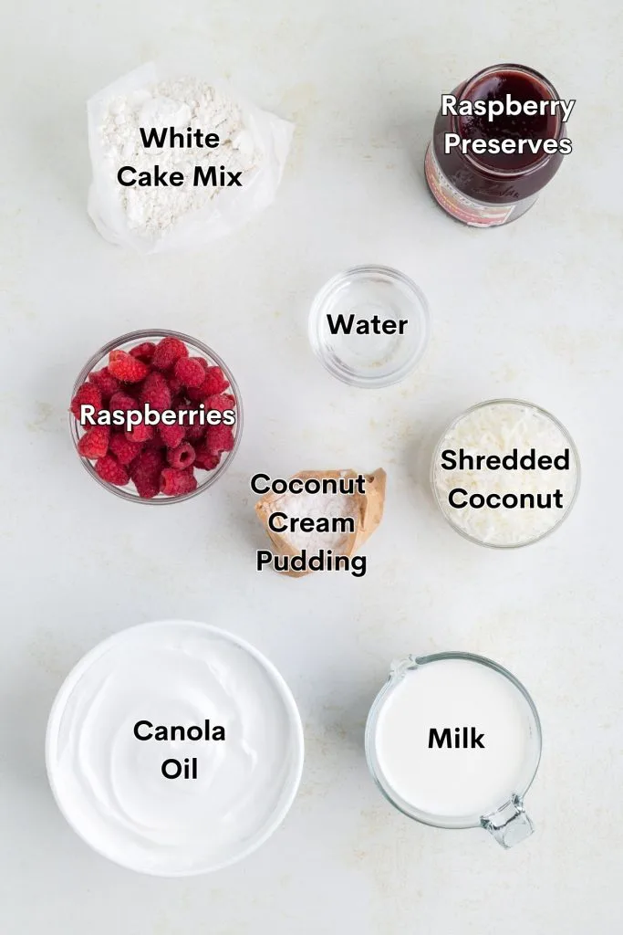 Ingredients such as cake mix, raspberry preserves, coconut cream pudding, cool whip, coconut, and raspberries displayed on the counter.