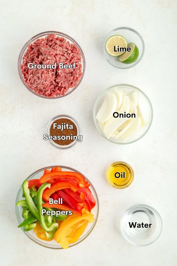 Ingredients such as ground beef, onion, bell peppers and seasoning laid out on the counter.