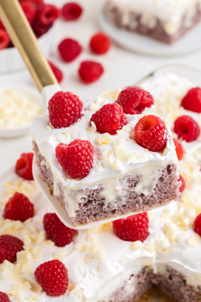 Slice of raspberry white chocolate poke cake with fresh raspberries.
