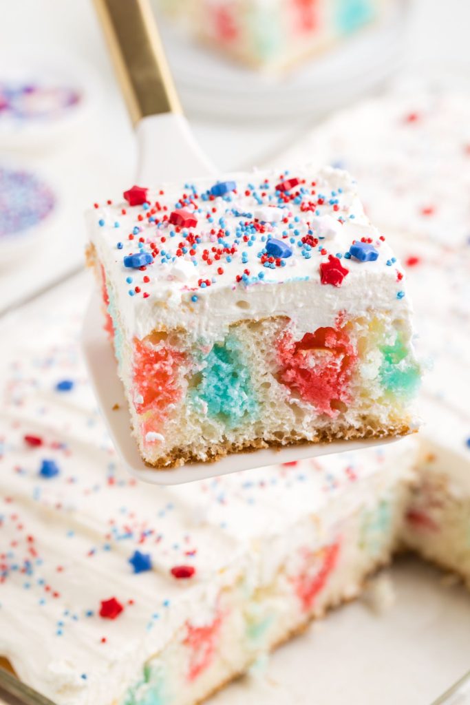 Slice of 4th of July poke cake with red and blue jello being removed from the pan. 