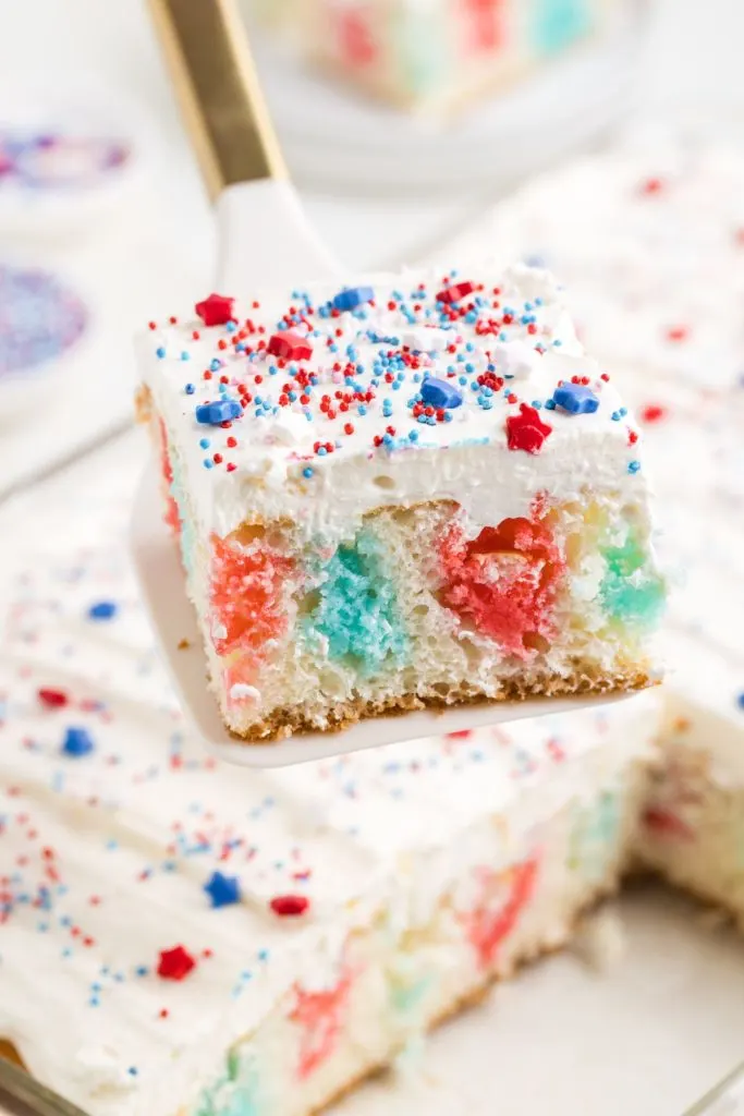 Slice of 4th of July poke cake with red and blue jello being removed from the pan. 