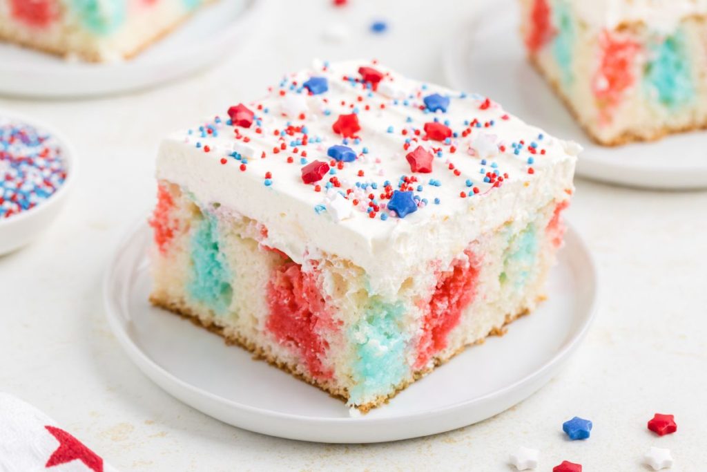 Slice of red, white and blue Jello poke cake on a plate with sprinkles.