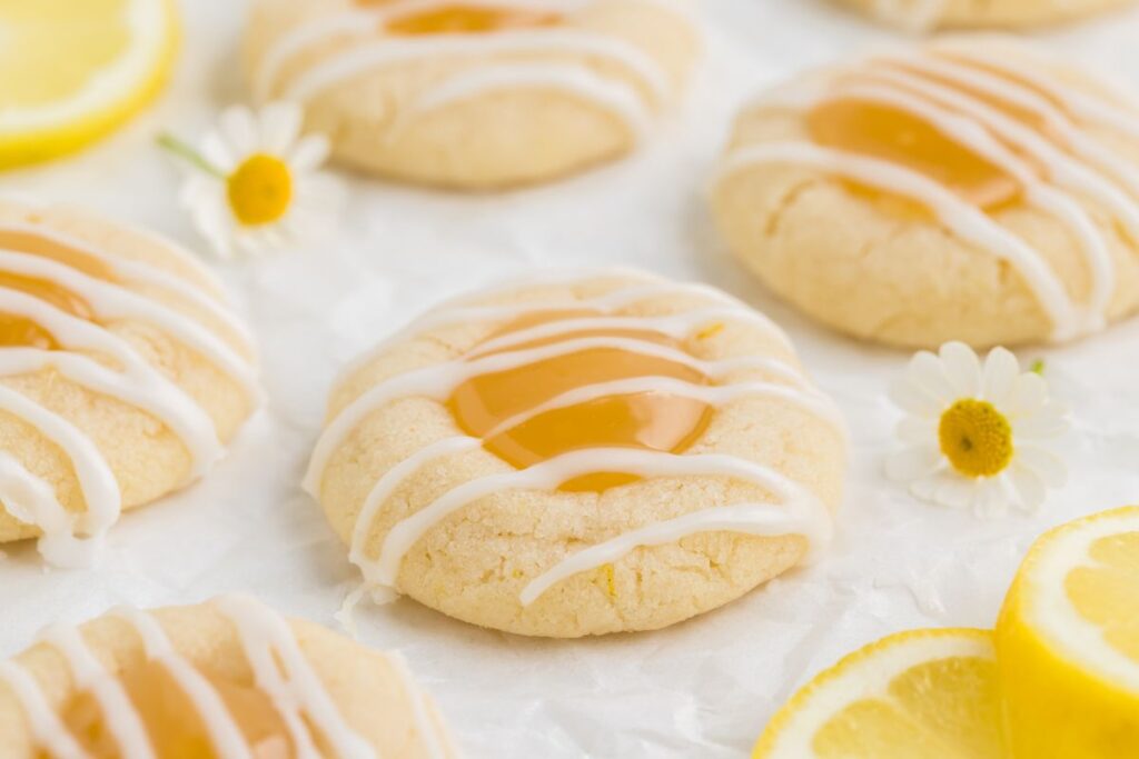 Lemon thumbprint cookies with lemon curb arranged on parchment paper.