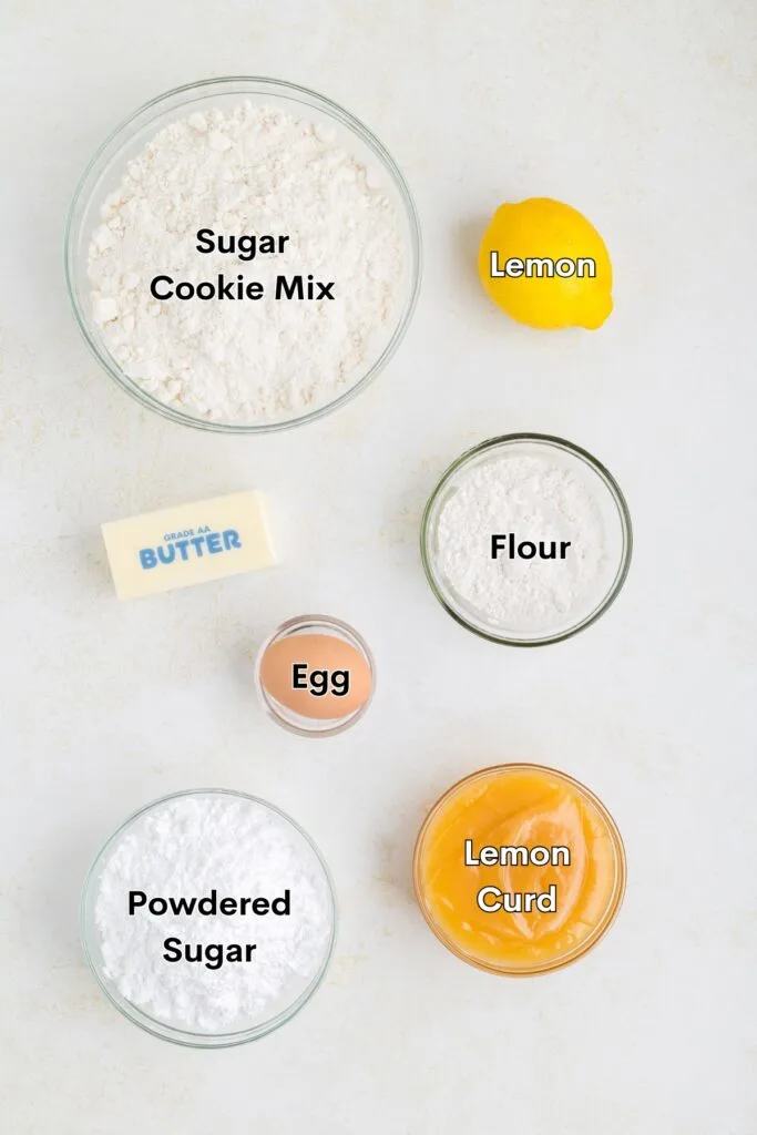 Ingredients such as cookie mix, lemon, flour, egg, butter, powdered sugar, and lemon curd displayed on the counter.