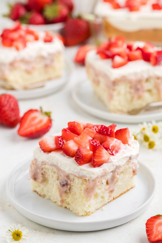 Slice of strawberry cheesecake poke cake with fresh strawberries.