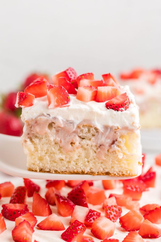 Slice of cheesecake poke cake covered in diced strawberries being removed from the pan.