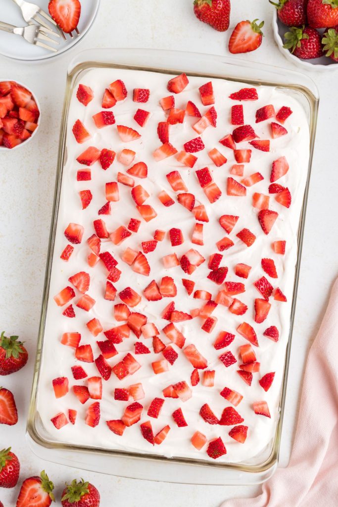 Strawberry cheesecake poke cake topped with cheesecake pudding whipped topping and fresh strawberries.