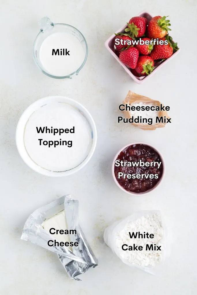 Ingredients such as white cake mix, cream cheese, strawberry preserves, pudding mix, milk, whipped topping, and fresh strawberries displayed on the counter.