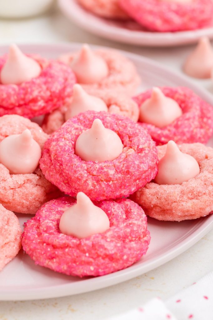 Pink strawberry cake mix cookies with Strawberry chocolate kisses piled on a plate.