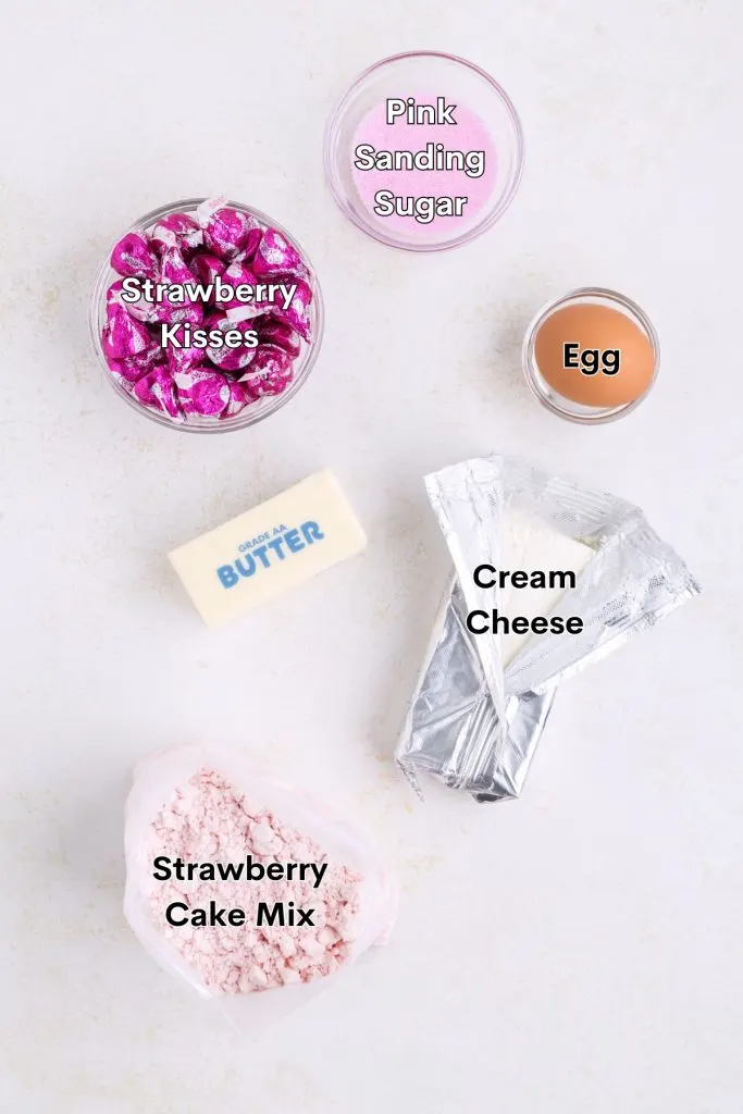 Ingredients like strawberry cake mix, butter, egg,  cream cheese, sanding sugar, and strawberry ice cream cone kisses displayed on the counter.