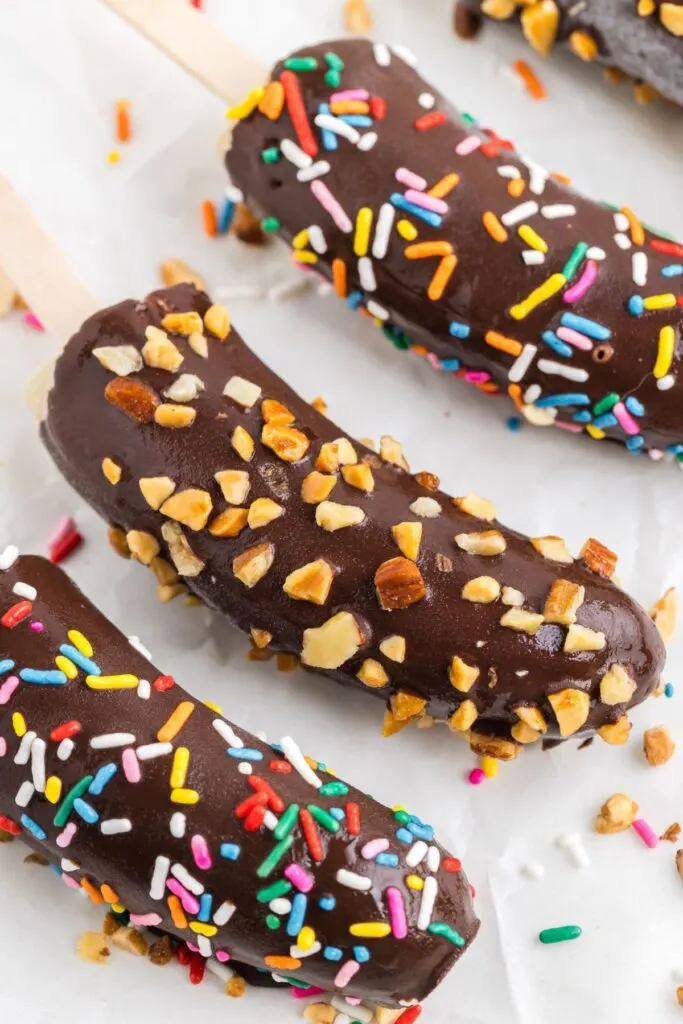 Chocolate banana popsicles with chopped nuts and rainbow sprinkles.