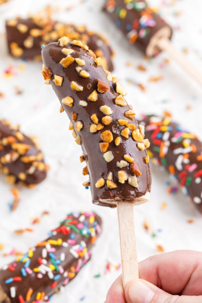 Banana on a popsicle stick covered in chocolate and chopped nuts.