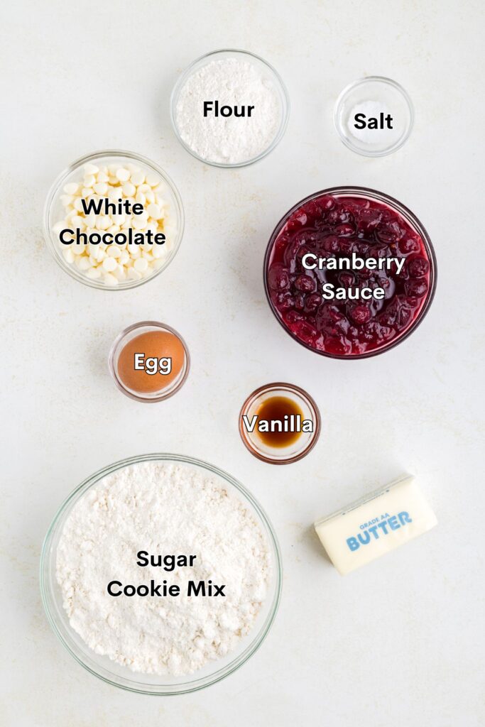 Ingredients such as sugar cookie dough, flour, egg, butter, vanilla, salt, cranberry sauce, and white chocolate displayed on the counter.