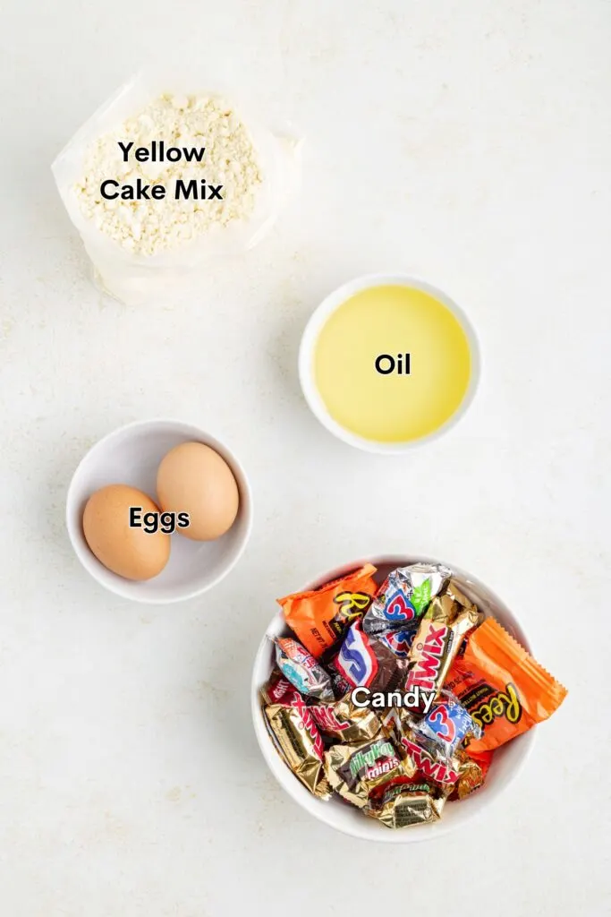 Ingredients such as yellow cake mix, eggs, oil and Halloween candy on the counter.