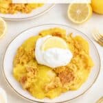 Plate of 3 Ingredient Lemon Dump Cake with whipped cream, lemon slice, fresh lemons, and a gold fork.