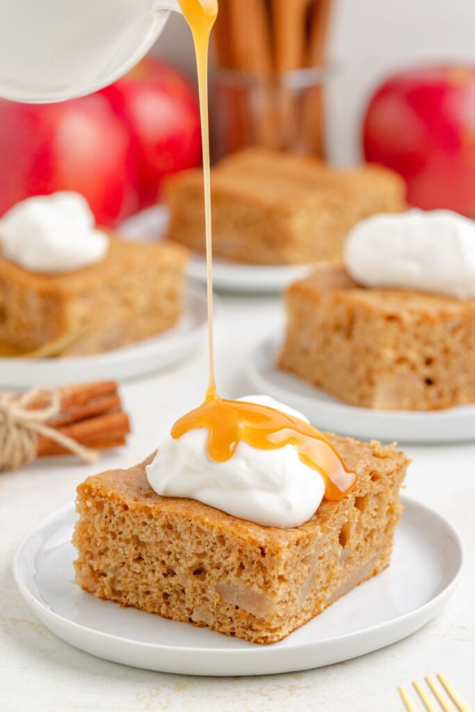 Three ingredient apple cake topped with whipped cream being drizzled with caramel sauce.