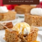 Square slice of apple spice cake with whipped cream and caramel on a white plate, more cake behind.
