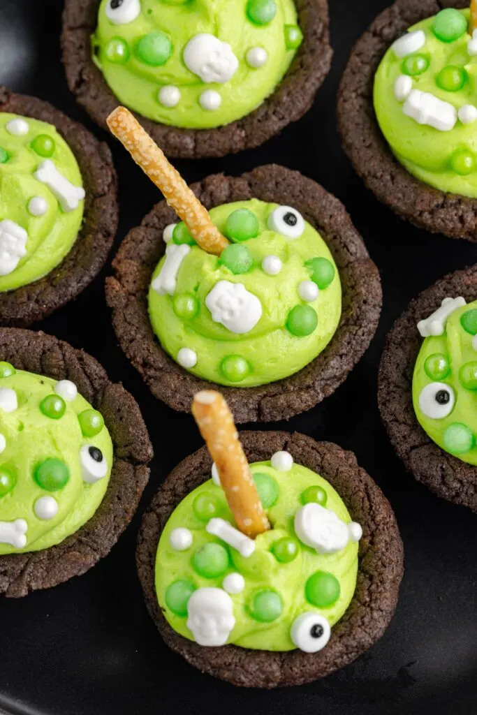 Cauldron cookies with green frosting and pretzel sticks.