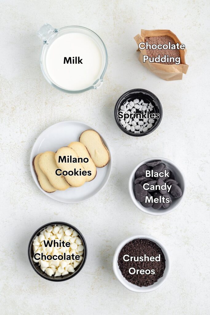 Ingredients such as pudding mix, milk, Oreo crumbs, white chocolate, black candy melts, cookies, and sprinkles displayed on the counter.