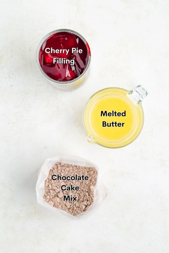 Ingredients such as cherry pie filling, chocolate cake mix, and melted butter displayed on the counter.