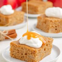 Three ingredient apple cake topped with whipped cream being drizzled with caramel sauce.