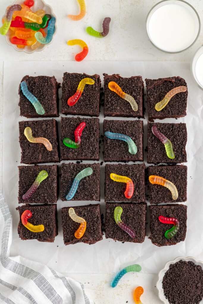 Dirt and worm brownies cut into squares arranged on parchment paper.