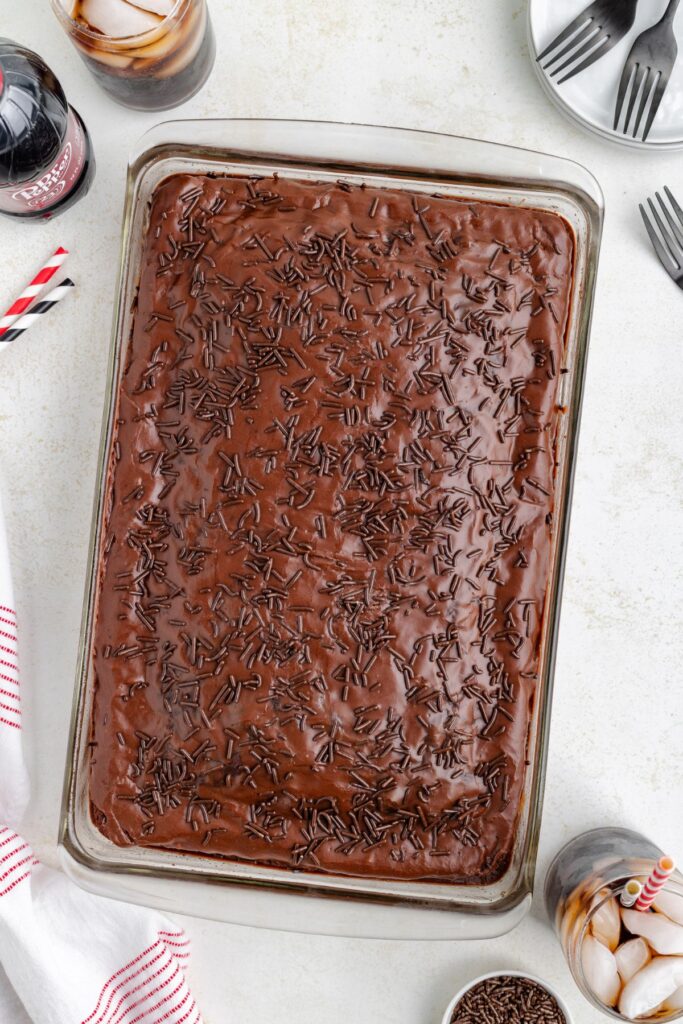 Chocolate Dr Pepper cake in a 9x13-inch cake pan covered in chocolate frosting and chocolate sprinkles.