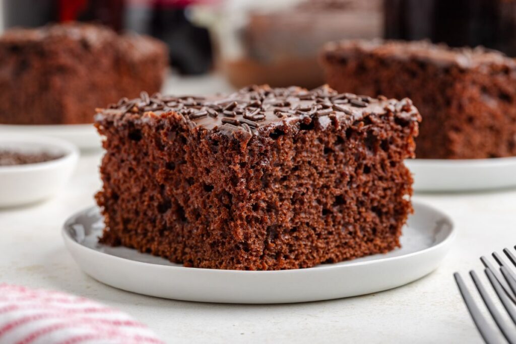 Slice of chocolate Dr Pepper cake with chocolate frosting and sprinkles on a white plate.