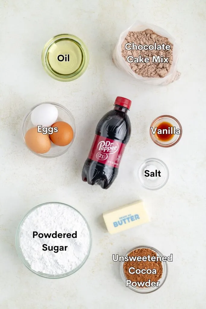 Ingredients such as chocolate cake mix, eggs, oil, Dr Pepper, powdered sugar, butter, cocoa powder, salt, and vanilla arranged on the counter.