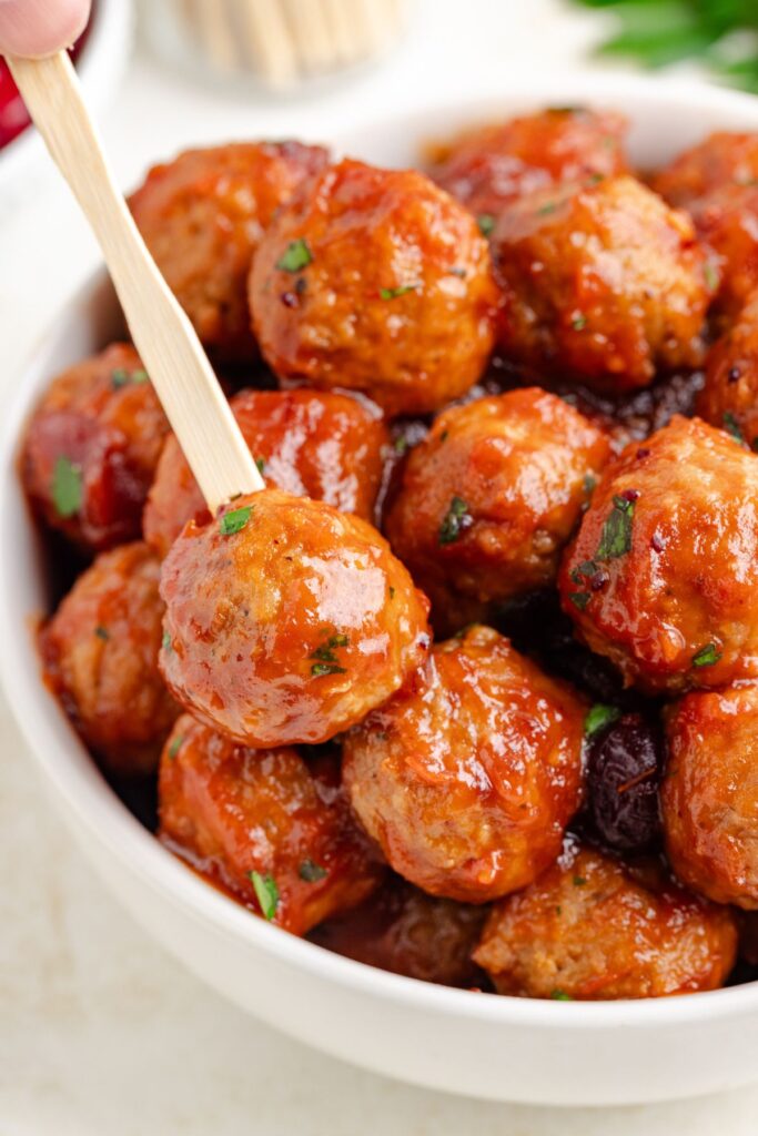 A 3-ingredient cranberry meatball in a bowl stabbed with a toothpick. 