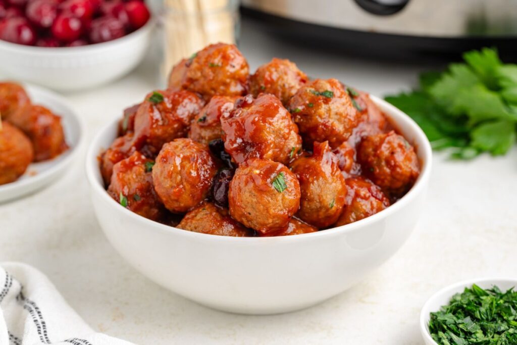 A bowl full of cranberry meatballs on the counter with a slow cooker in the background.