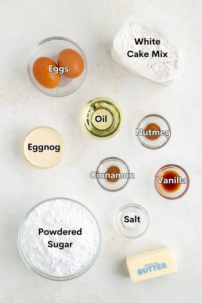 Ingredients such as cake mix, eggs, oil, eggnog, powdered sugar, butter, vanilla, and spices arranged on the counter.