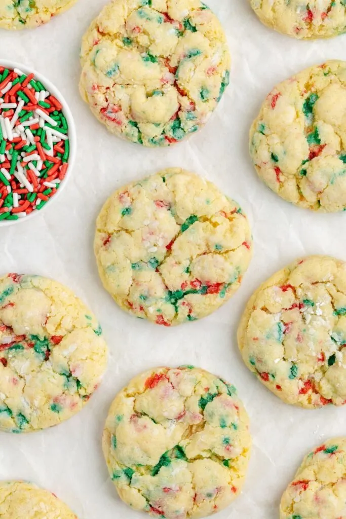 Gooey butter cookies with red, green and white sprinkles arranged on a piece of parchment paper. 