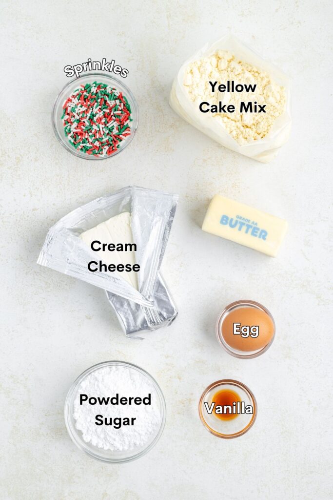 Ingredients such as yellow cake mix, cream cheese, butter, egg, vanilla, powdered sugar, and sprinkles displayed in bowls.