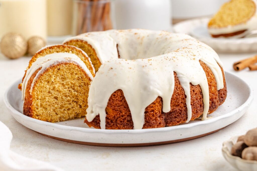 Eggnog bundt cake on a platter with some slices cut.