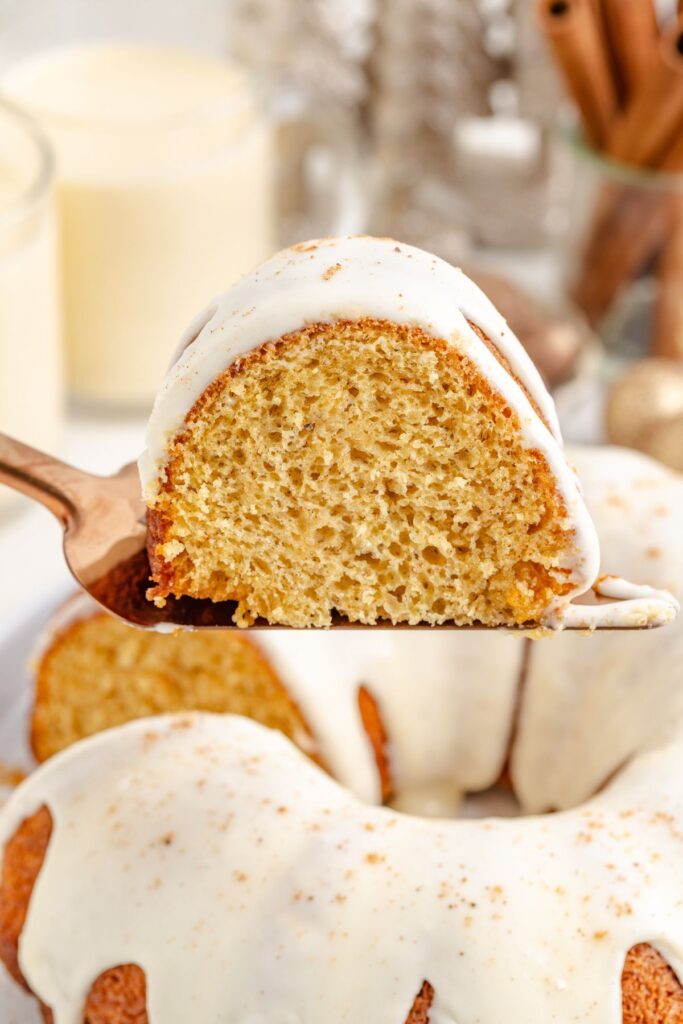 Slice of cake with eggnog glaze being removed from the whole cake.